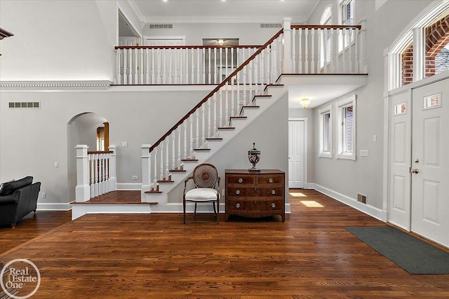 foyer entrance with stairs, arched walkways, visible vents, and a towering ceiling