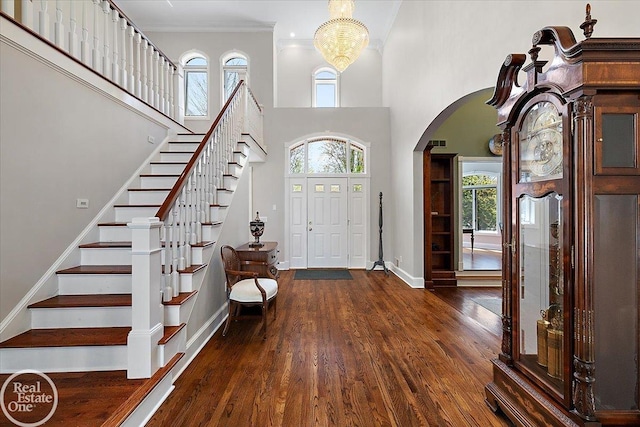 entrance foyer featuring stairs, arched walkways, baseboards, and wood finished floors
