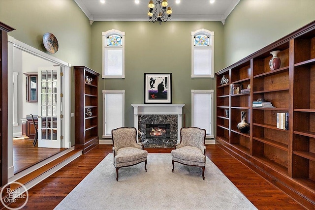 living area featuring a towering ceiling, dark wood-type flooring, a chandelier, ornamental molding, and a premium fireplace