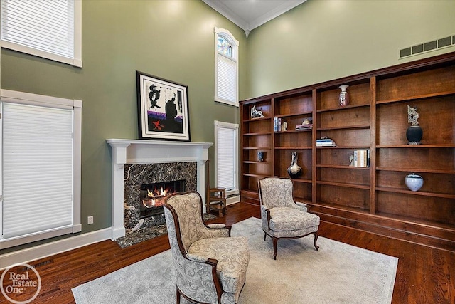 sitting room with visible vents, ornamental molding, a towering ceiling, wood finished floors, and a high end fireplace