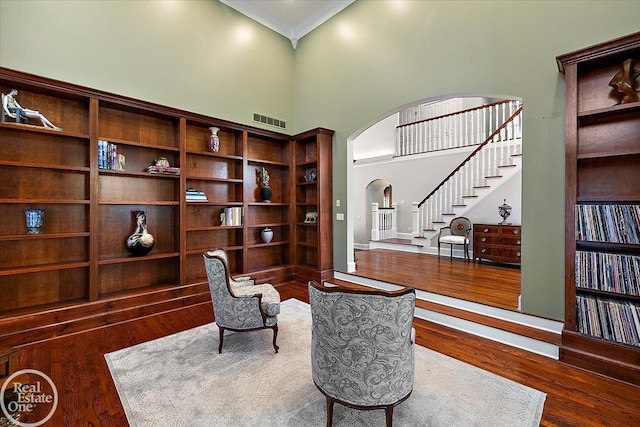 sitting room featuring arched walkways, stairs, wood finished floors, a towering ceiling, and ornamental molding