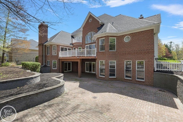 rear view of property featuring brick siding, a shingled roof, a patio area, and a wooden deck