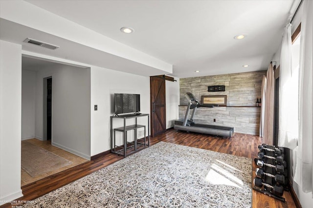 exercise area featuring visible vents, wood finished floors, a barn door, baseboards, and recessed lighting
