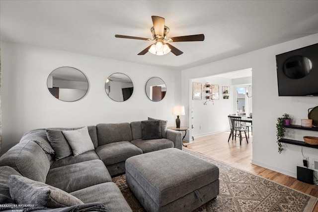 living area with baseboards, a ceiling fan, and wood finished floors