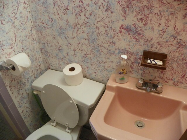 bathroom featuring a sink, toilet, and wallpapered walls