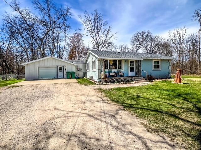 single story home with a garage, dirt driveway, covered porch, and a front lawn