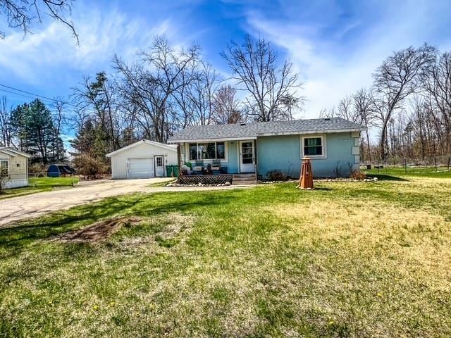ranch-style home with a garage, covered porch, driveway, a front yard, and an outbuilding