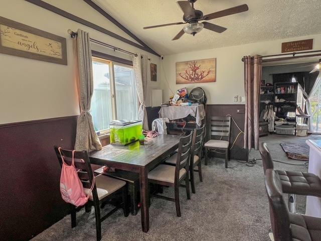 carpeted dining room featuring a ceiling fan, a textured ceiling, and vaulted ceiling
