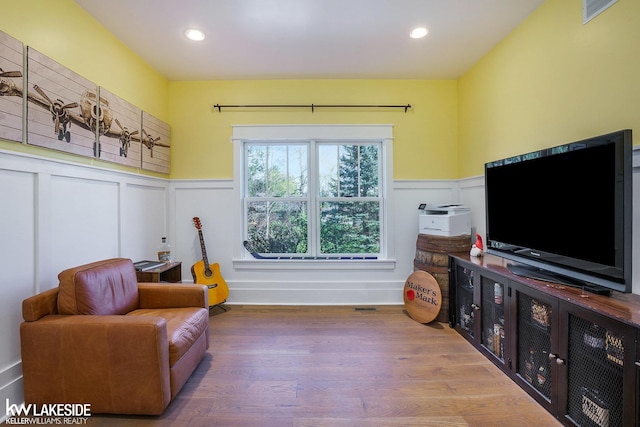 sitting room featuring a decorative wall, visible vents, wood finished floors, and a wainscoted wall