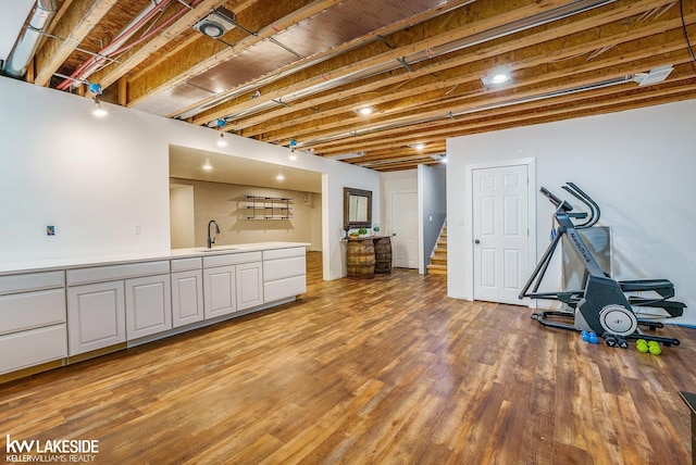 finished below grade area with a sink, indoor wet bar, light wood-type flooring, and stairs
