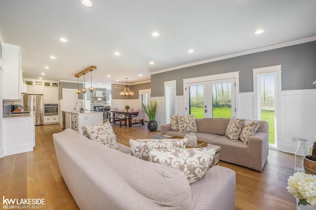 living area with wood-type flooring, an inviting chandelier, ornamental molding, and a wainscoted wall