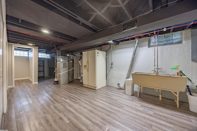 basement with a sink, white refrigerator with ice dispenser, and wood finished floors
