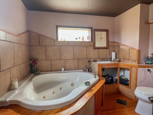 full bath with toilet, a tub with jets, and wood finished floors