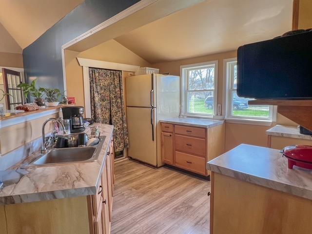 kitchen featuring freestanding refrigerator, a sink, lofted ceiling, and light wood-style flooring