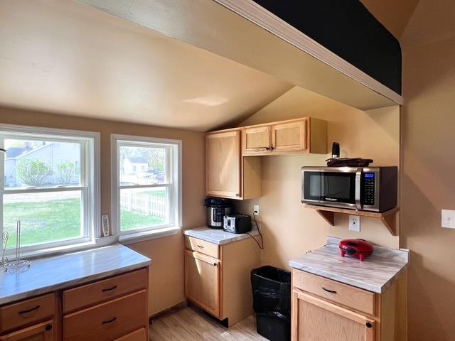 kitchen with lofted ceiling, light brown cabinets, light countertops, stainless steel microwave, and light wood finished floors