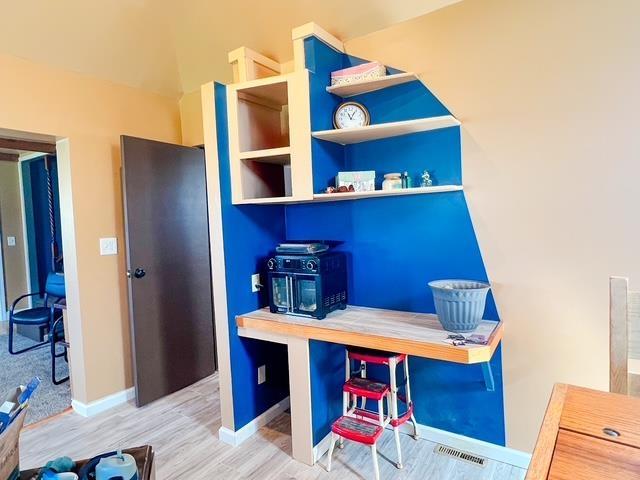 office featuring baseboards, visible vents, wood finished floors, and a wood stove