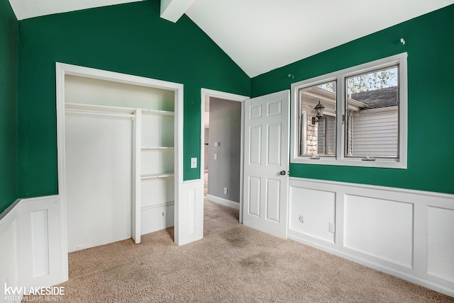 unfurnished bedroom with carpet floors, a closet, wainscoting, a decorative wall, and lofted ceiling with beams