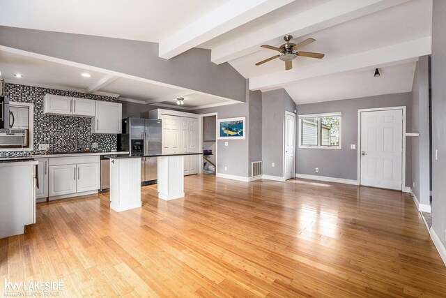 kitchen with a ceiling fan, a kitchen island, visible vents, open floor plan, and vaulted ceiling with beams