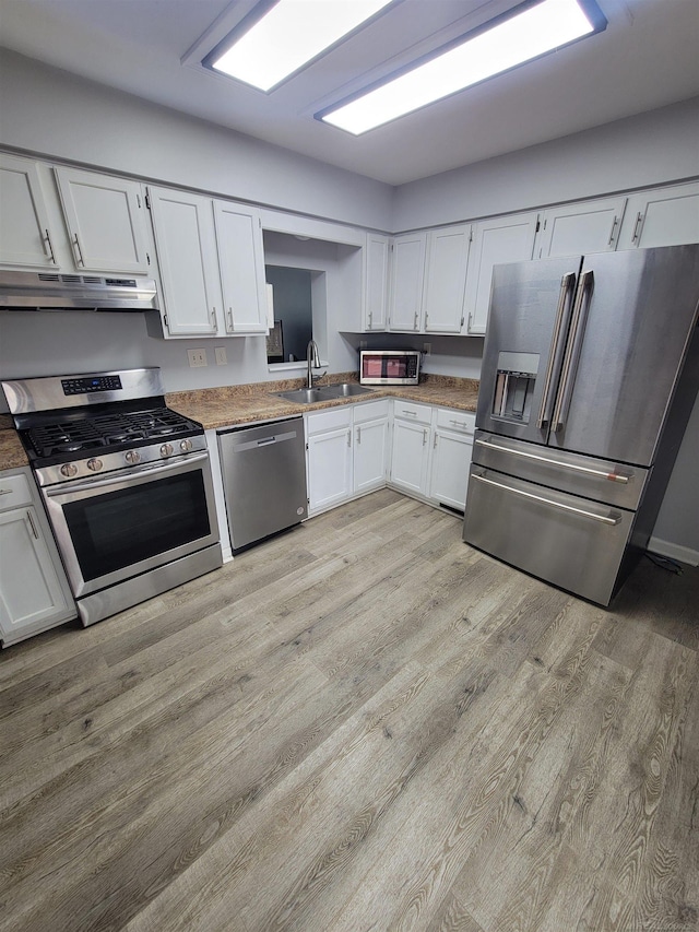 kitchen with under cabinet range hood, white cabinets, a sink, light wood finished floors, and appliances with stainless steel finishes
