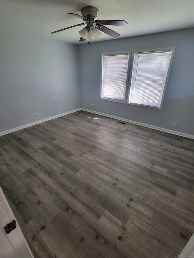 empty room with ceiling fan, dark wood finished floors, and baseboards