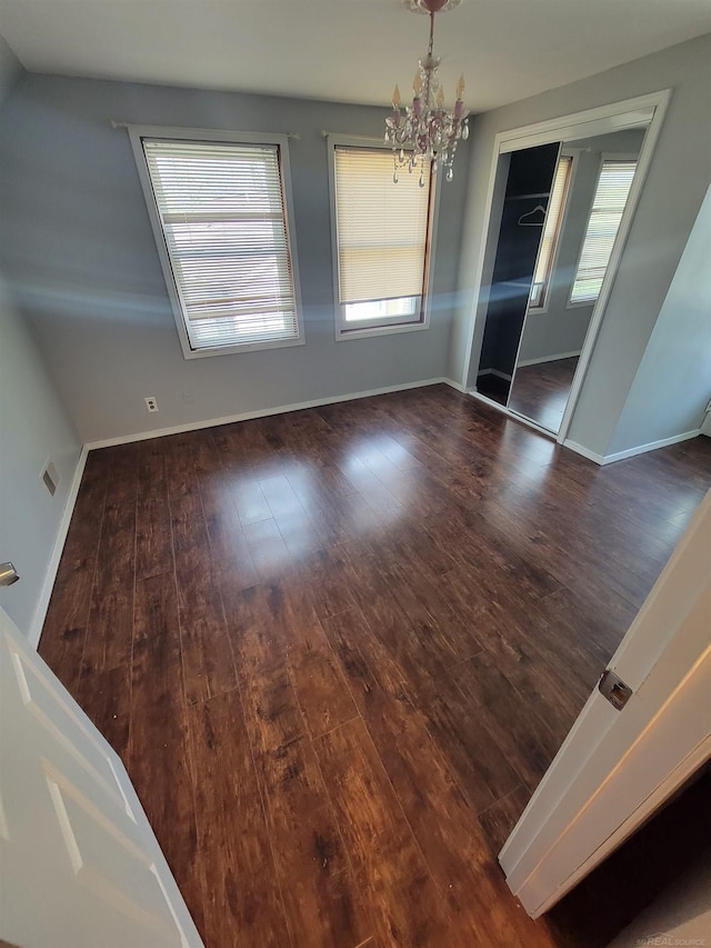 unfurnished dining area with baseboards, a chandelier, hardwood / wood-style flooring, and visible vents