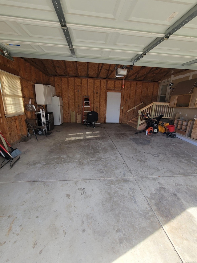 garage with a garage door opener, wooden walls, and freestanding refrigerator