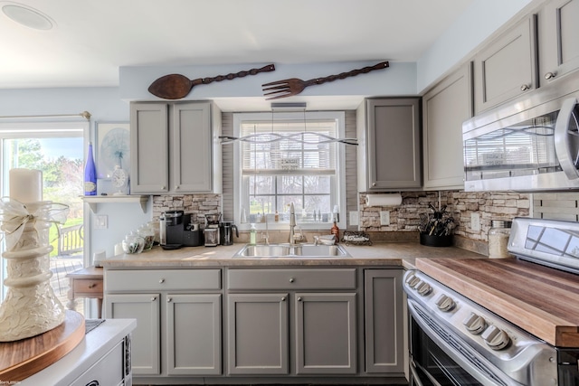 kitchen featuring backsplash, stainless steel appliances, gray cabinets, and a sink