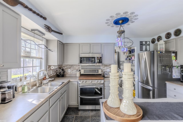 kitchen featuring hanging light fixtures, appliances with stainless steel finishes, a sink, light countertops, and decorative backsplash