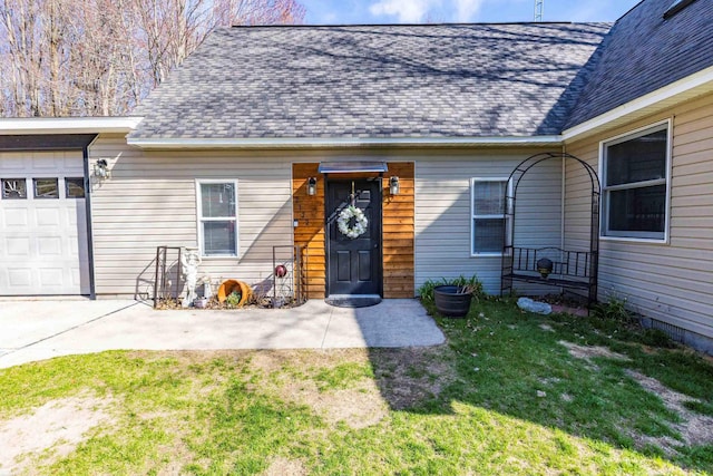 view of exterior entry featuring roof with shingles, an attached garage, and a yard