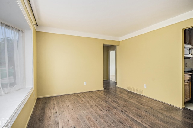 empty room featuring baseboards, dark wood finished floors, and visible vents