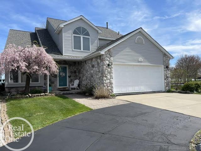 traditional home with an attached garage, driveway, stone siding, and a front lawn