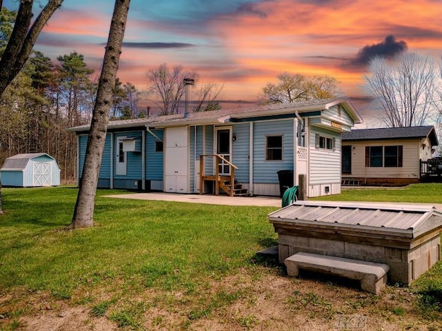 back of house at dusk featuring an outdoor structure, a yard, and a storage shed