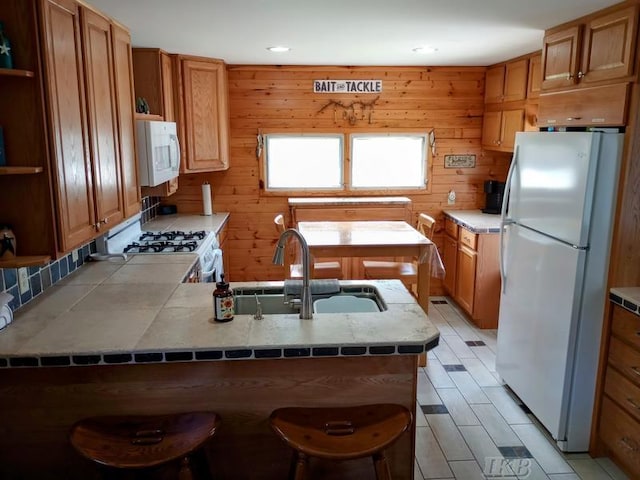 kitchen with open shelves, a sink, white appliances, a peninsula, and a kitchen bar