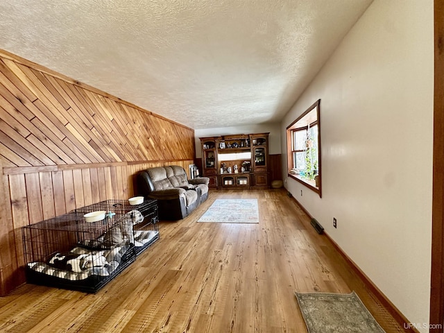 living area featuring wood walls, baseboards, hardwood / wood-style flooring, and a textured ceiling