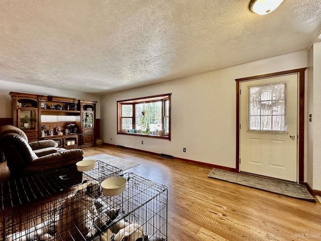 living area featuring baseboards, light wood finished floors, a textured ceiling, and visible vents