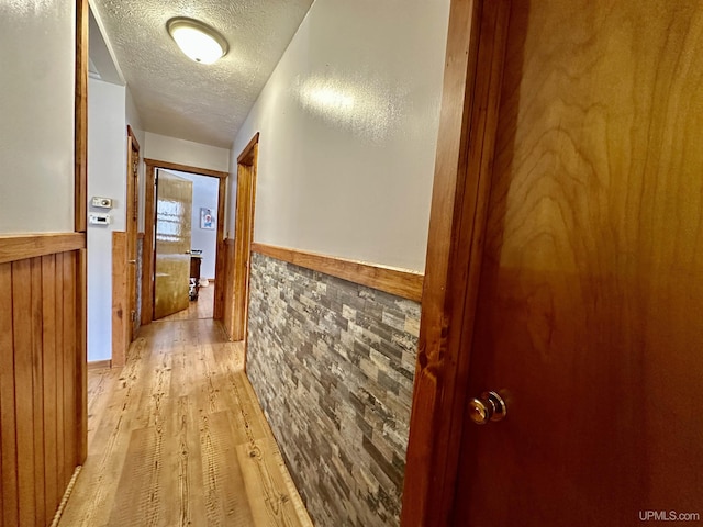 hallway featuring wainscoting, light wood-type flooring, and a textured ceiling
