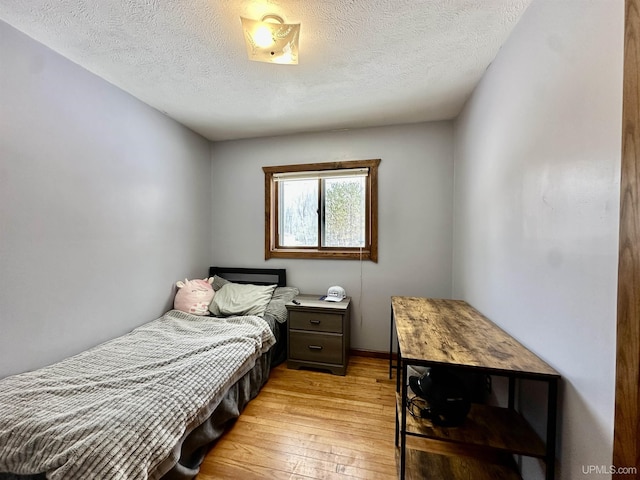 bedroom with baseboards, light wood finished floors, and a textured ceiling
