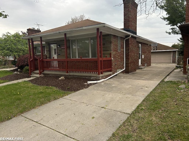 view of front of property featuring an outdoor structure, covered porch, a chimney, brick siding, and a detached garage