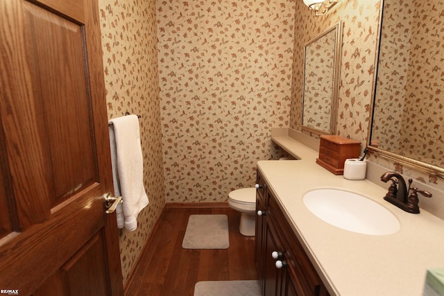 bathroom with vanity, wood finished floors, toilet, baseboards, and wallpapered walls