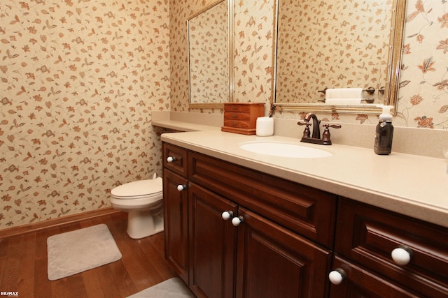 bathroom featuring vanity, toilet, wallpapered walls, and wood finished floors