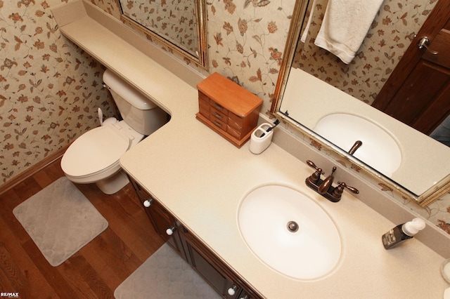 bathroom with toilet, wallpapered walls, wood finished floors, and vanity