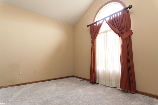 empty room featuring baseboards, lofted ceiling, and light colored carpet