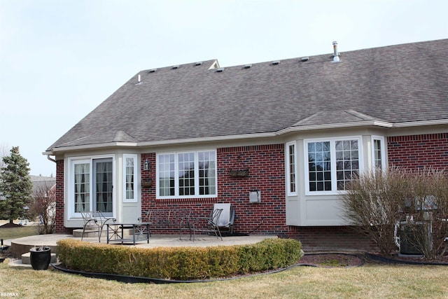 back of house with brick siding, a shingled roof, a patio area, and a lawn