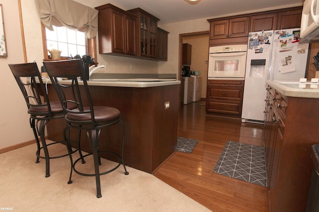 kitchen with dark wood-style flooring, white appliances, a peninsula, a kitchen bar, and glass insert cabinets