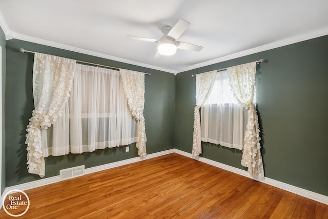 spare room featuring a ceiling fan, visible vents, crown molding, wood finished floors, and baseboards