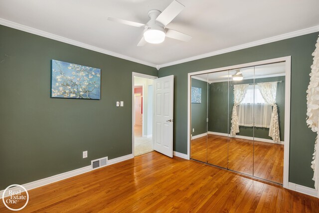 unfurnished bedroom with crown molding, baseboards, wood finished floors, visible vents, and a closet