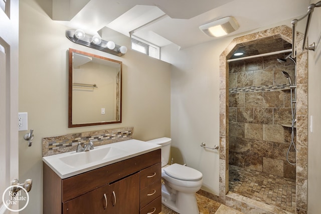 bathroom with toilet, tiled shower, and vanity