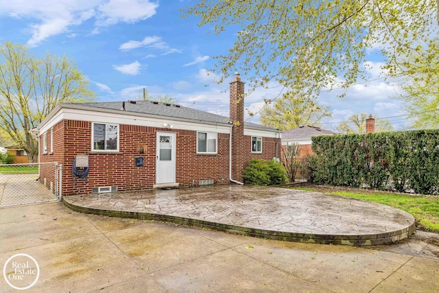 rear view of house featuring brick siding, fence, a chimney, and a patio