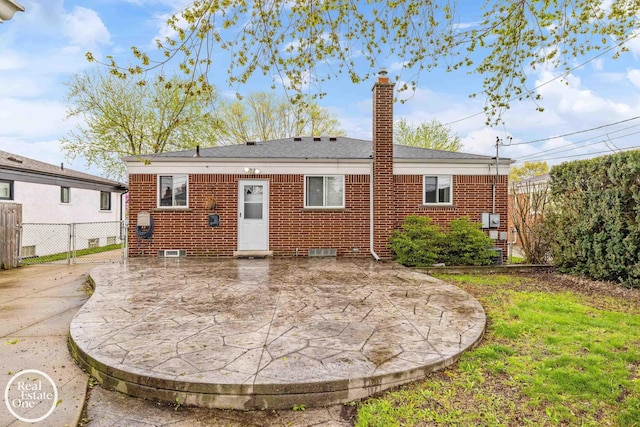 rear view of house with brick siding, a patio area, fence, and a chimney