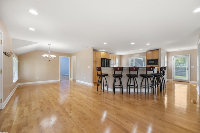 kitchen featuring an inviting chandelier, light brown cabinetry, a breakfast bar, and black appliances